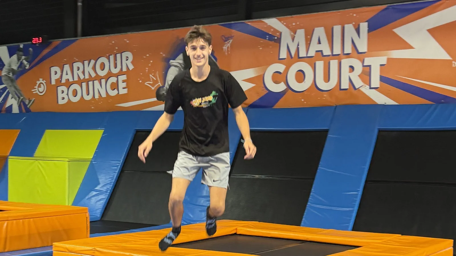 Un adolescent saute sur un trampoline du parc New Jump, devant les panneaux Parkour Bounce et Main Court